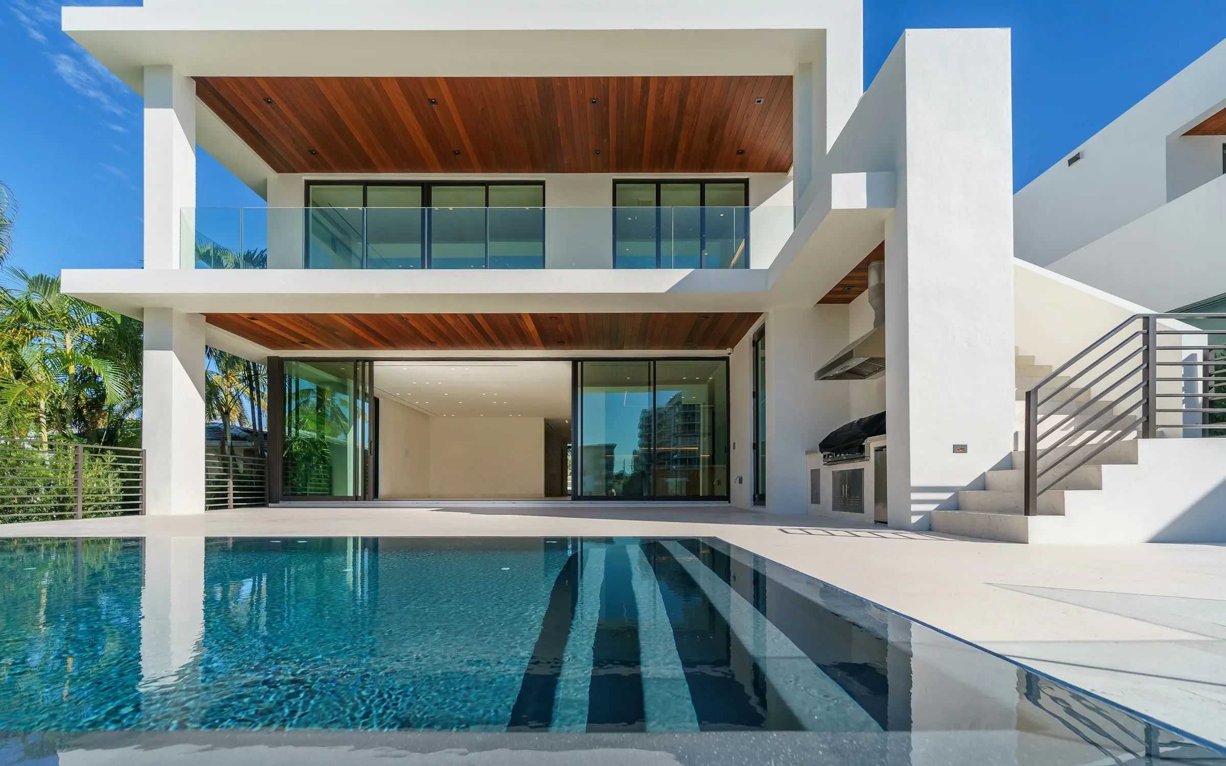 A modern white two-story house with a long in-ground pool across the whole back terrace